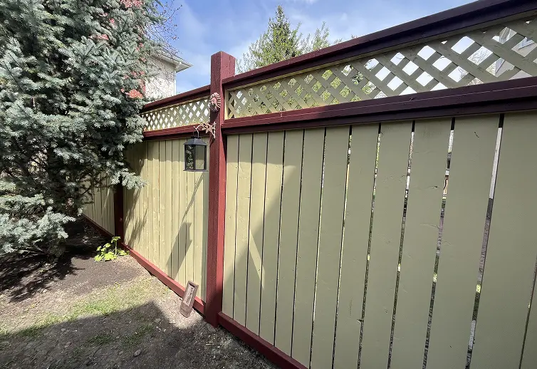 After fence painting service in Calgary featuring a modern two-tone design with light olive green panels and deep red trim.