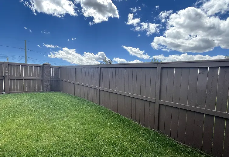 After solid color fence staining in Calgary presenting a uniform, clean dark brown protective finish on a backyard fence.