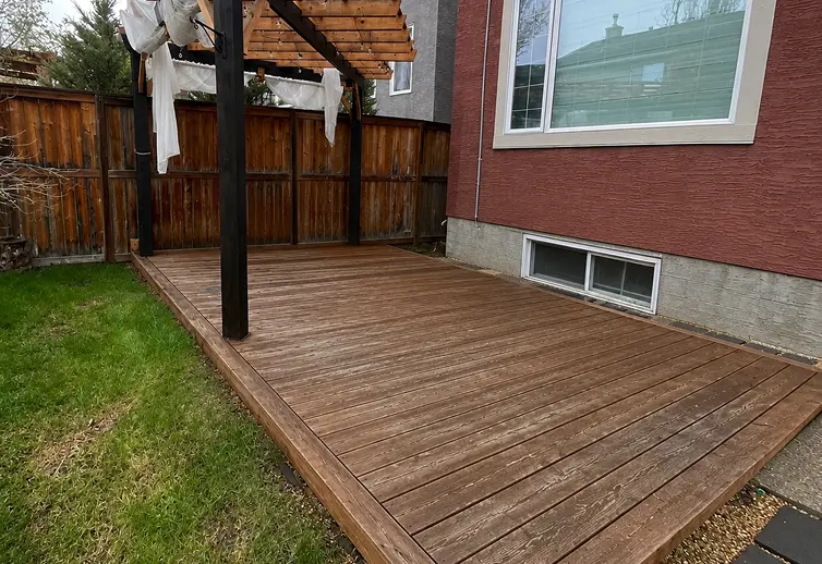 Before deck staining services in Calgary showing a weathered, faded brown wood deck in a backyard.