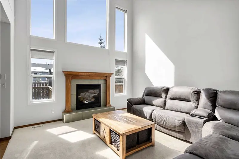 Multi-story residential living room painting by Color Works Painting featuring towering white walls, massive windows, and a central stone fireplace.
