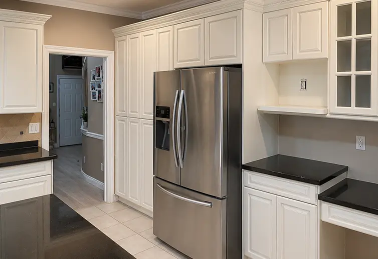 Calgary kitchen after cabinet painting with bright white cabinetry, black countertops, and a clean modern appearance.